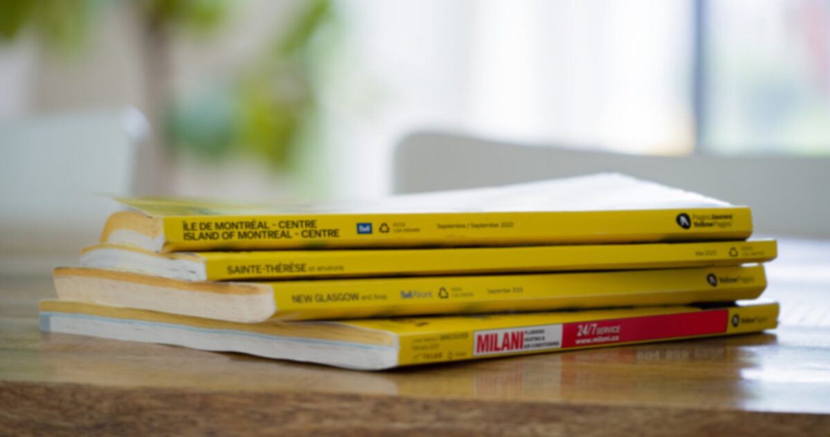 Exemplaire de l'annuaire Pages Jaunes posé à côté d'un smartphone affichant une recherche de professionnel